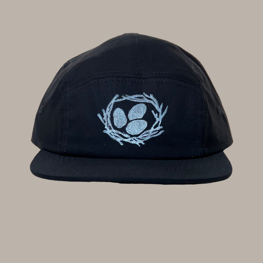 Black cap with a white egg print design on a beige background